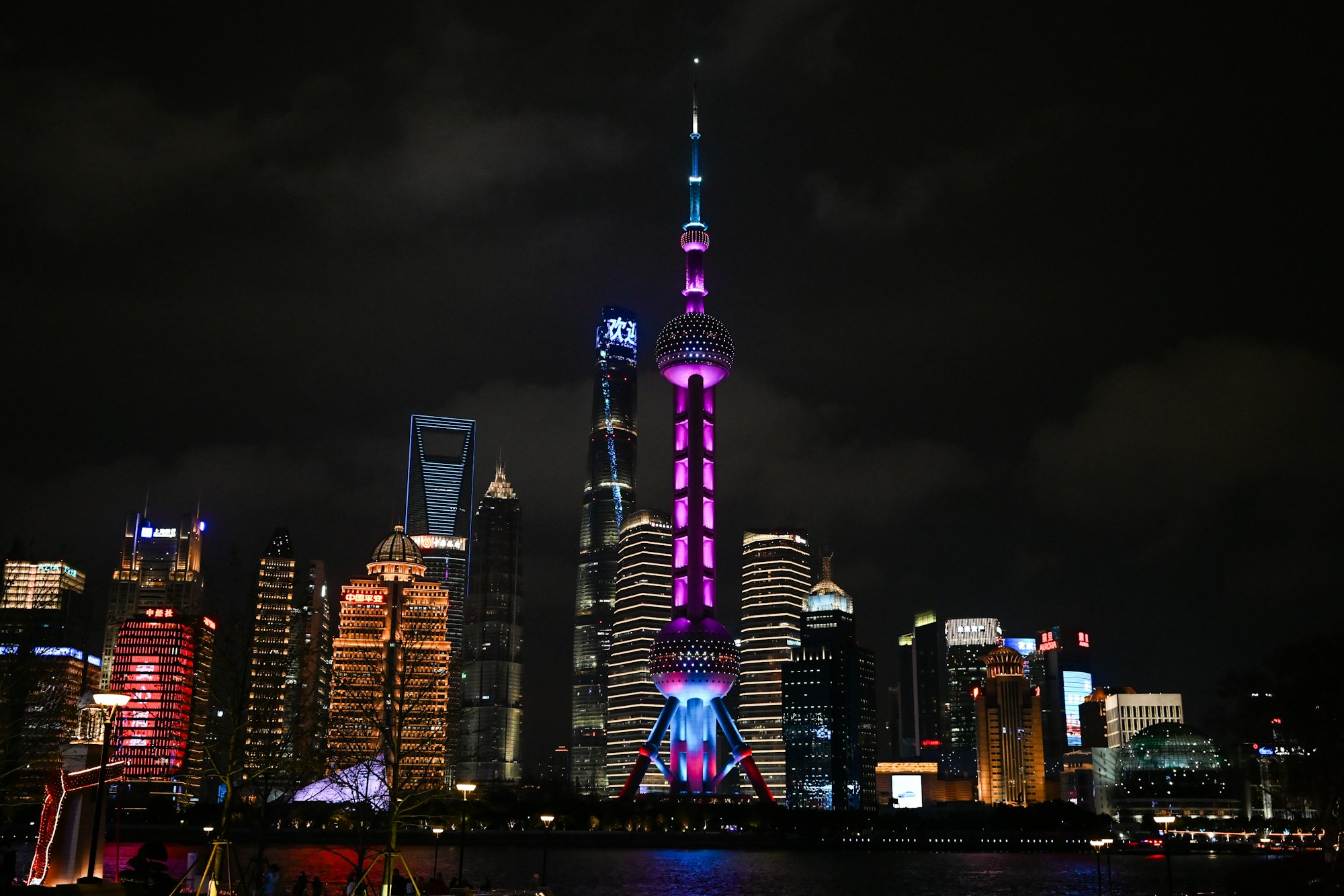 A Torre Pérola Oriental iluminada em roxo ao lado dos edifícios de Xangai à noite