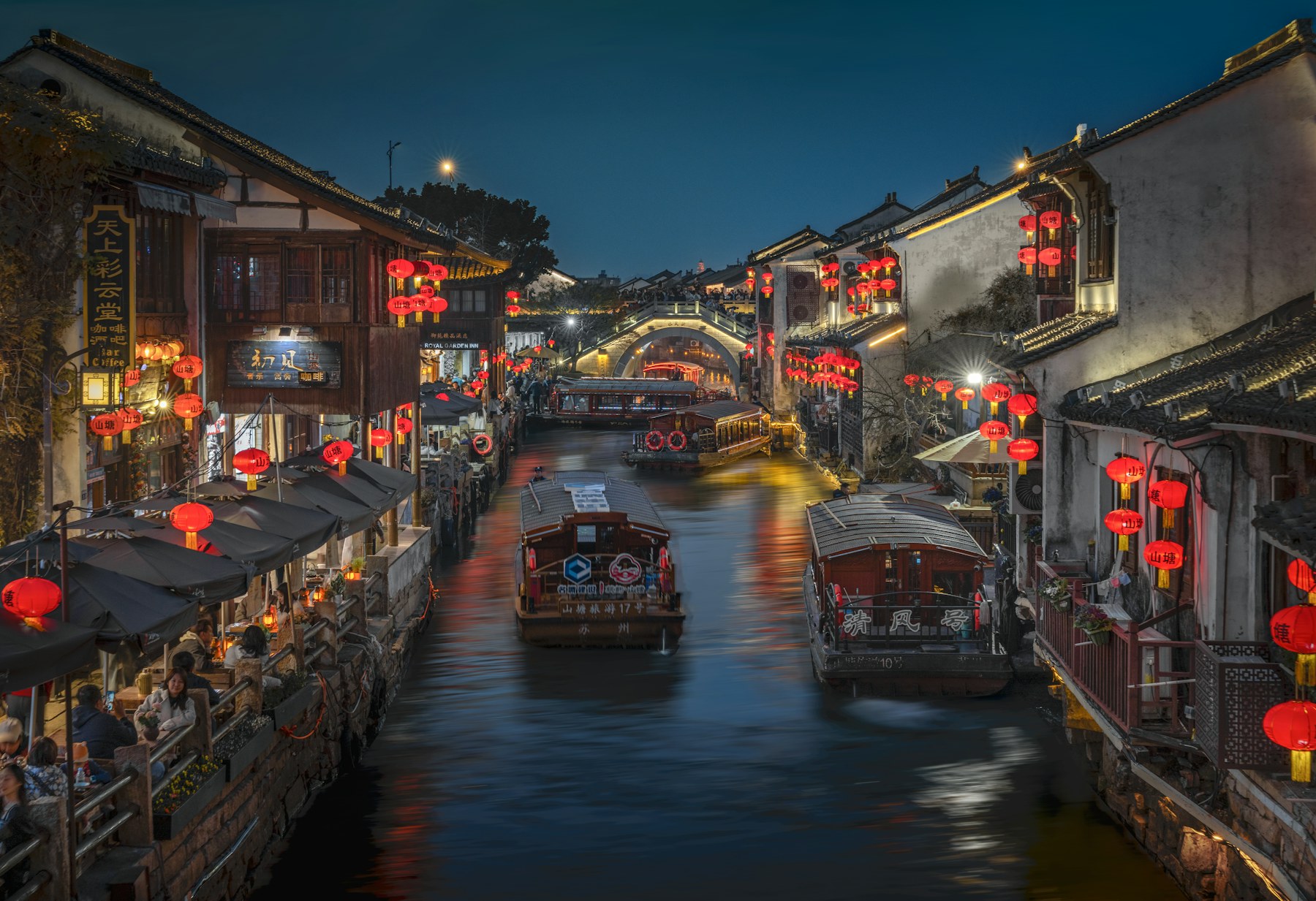 Lanternas vermelhas, barcos tradicionais e reflexos de tons quentes em um canal de Suzhou à noite